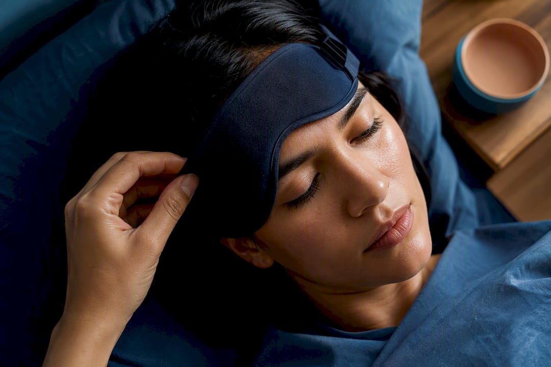 Hand adjusting contoured sleep mask in bedroom